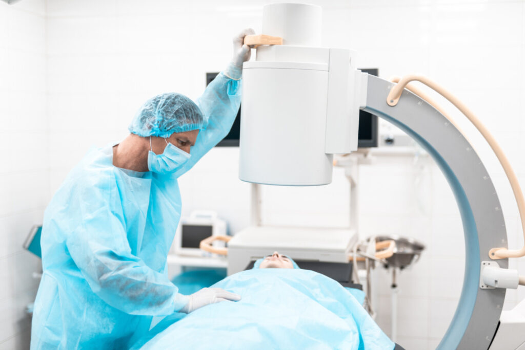 Professional doctor in medical uniform standing close to his patient and using C-arm machine